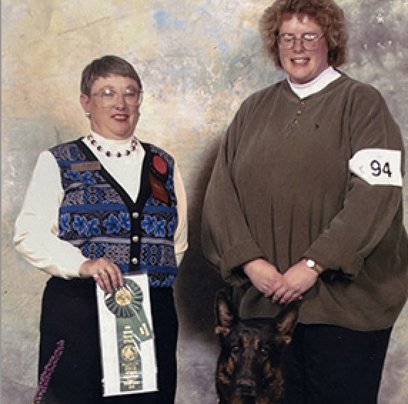 Obedience Judge displays winner's ribbon as exhibitor and dog standby.