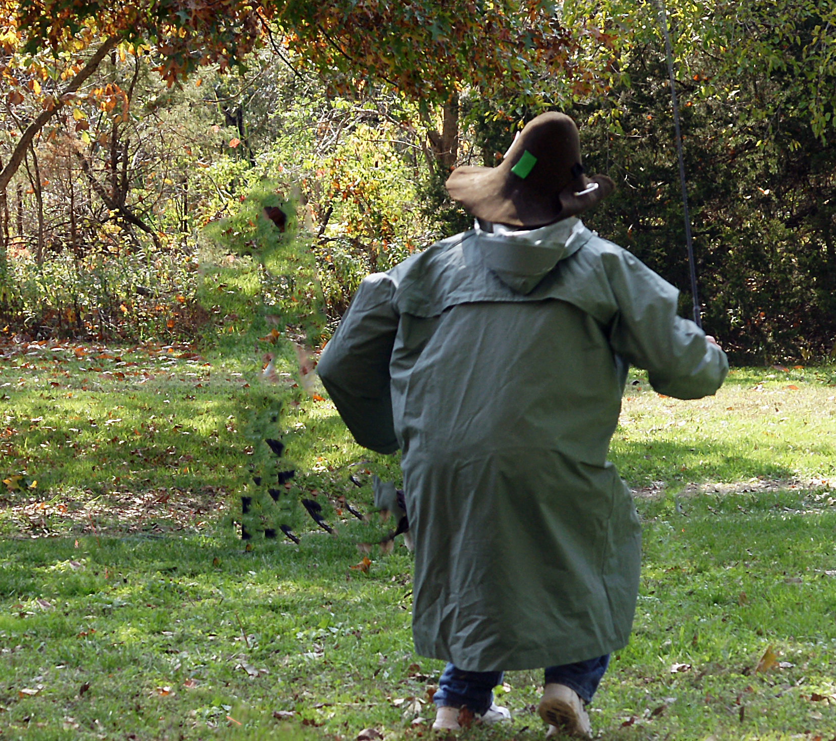 Man dressed in raincoat, wearing floppy hat runs toward dog and handler as final temperament test step.