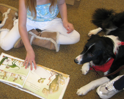 Girl sitting next to Border Collie with open book and her fingers pointing to text